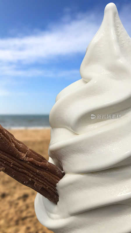 在阳光、沙滩和大海的模糊背景下，99片软冰淇淋配上白色香草口味的软冰淇淋/牛奶巧克力片，在炎热的阳光日子里，吃着不健康的冷小吃，让人感到凉爽